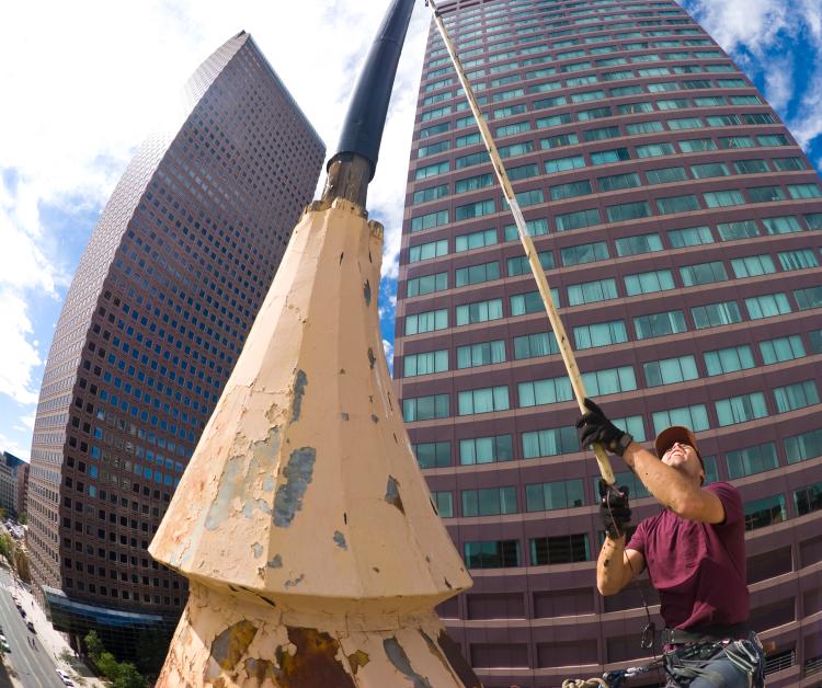 A worker is seen with a long pole, painting a flagpole in downtown Denver.