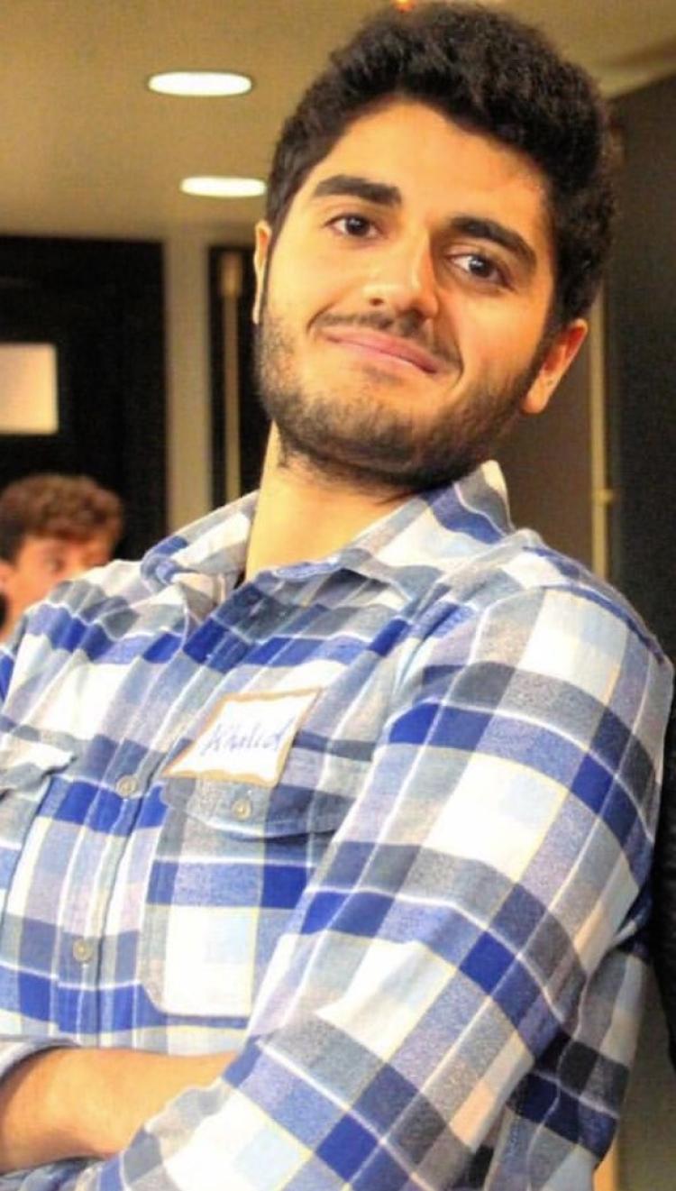 A portrait of Khalid AlAwadhi in a hallway. He is wearing a plaid long-sleeve shirt.