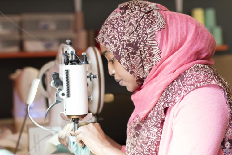 Hibo Ali Wehliye hovers intently over a sewing machine as she stitches green fabric.