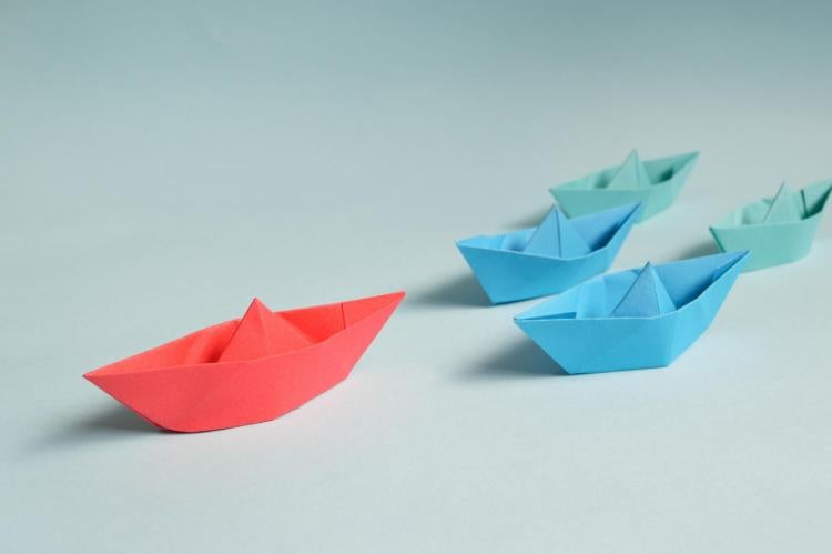 red paper boat leading other paper boats