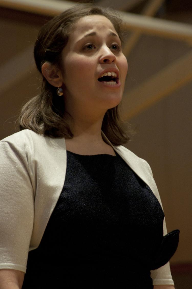Lia Bendix in a shite short-sleeve sweater and black dress singing/