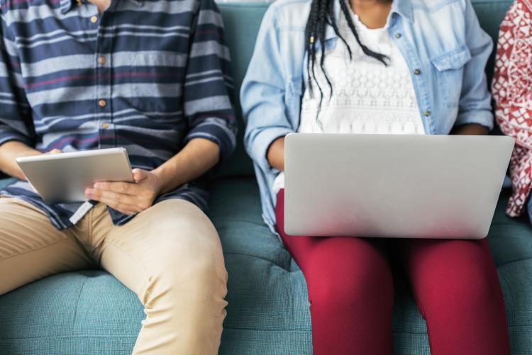 Man on tablet, woman on laptop sit next to each other