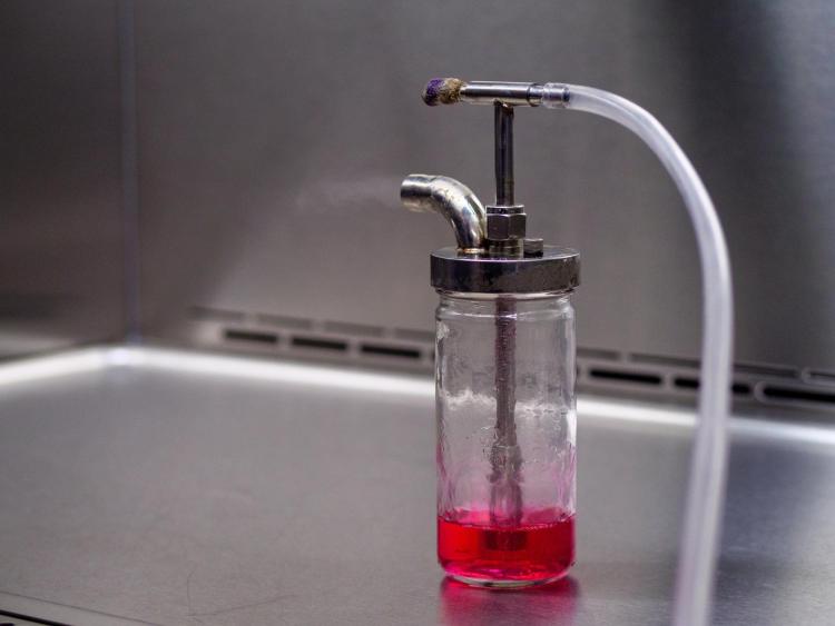 Bottle filled with red-colored sample media used to demonstrate aerosolization of the particles in the chamber