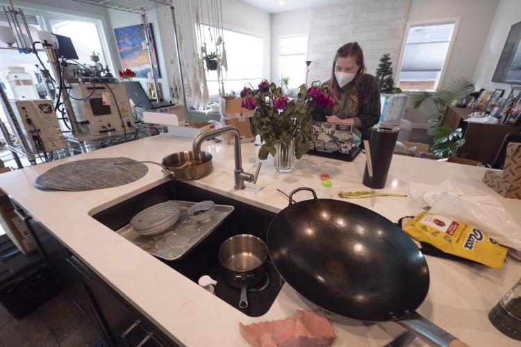 Woman sits at laptop in front of cluttered sink