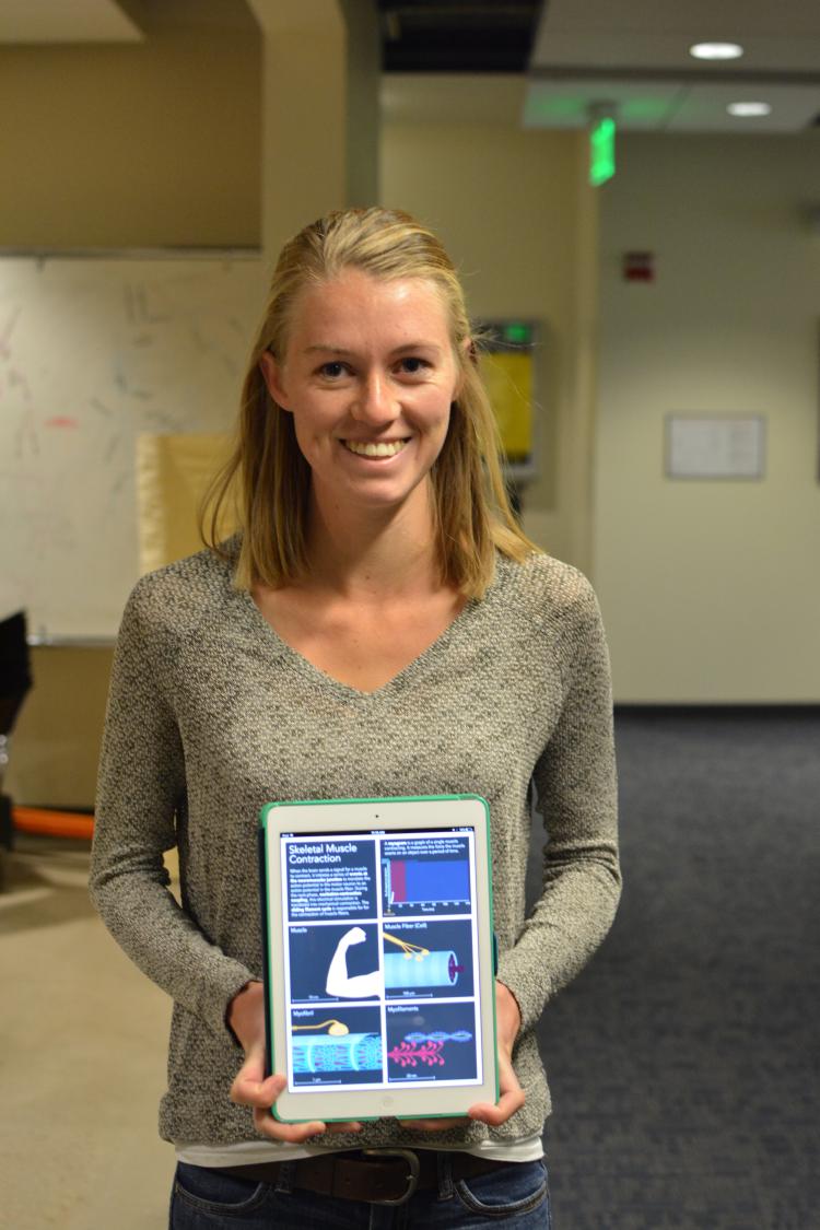 Megan Leahy dressed in a gray sweater, holds her interactive textbook in front of her.