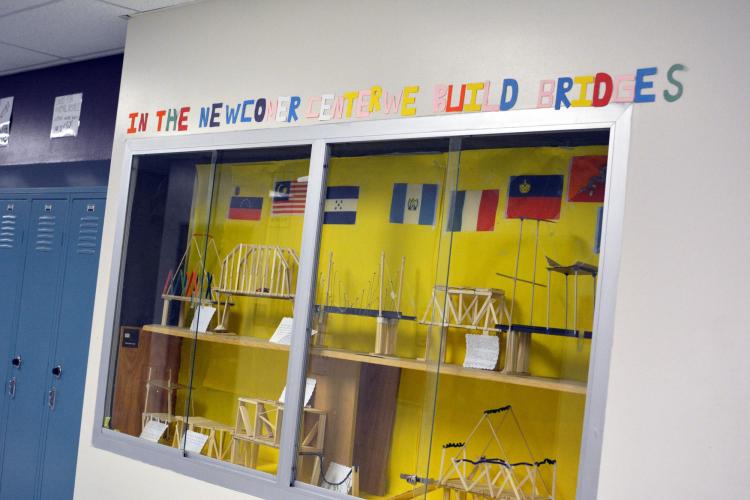 A glass display case reveals several models of bridges made out of wood. Above, colorful letters spell out: "In the newcomer center we build bridges."