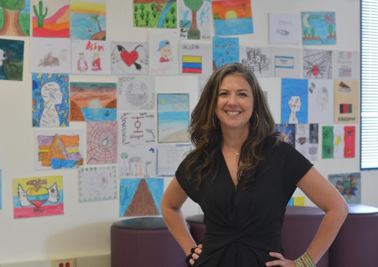 Woman stands in front of a wall with hand-drawn artwork on sheets of paper hanging behind her