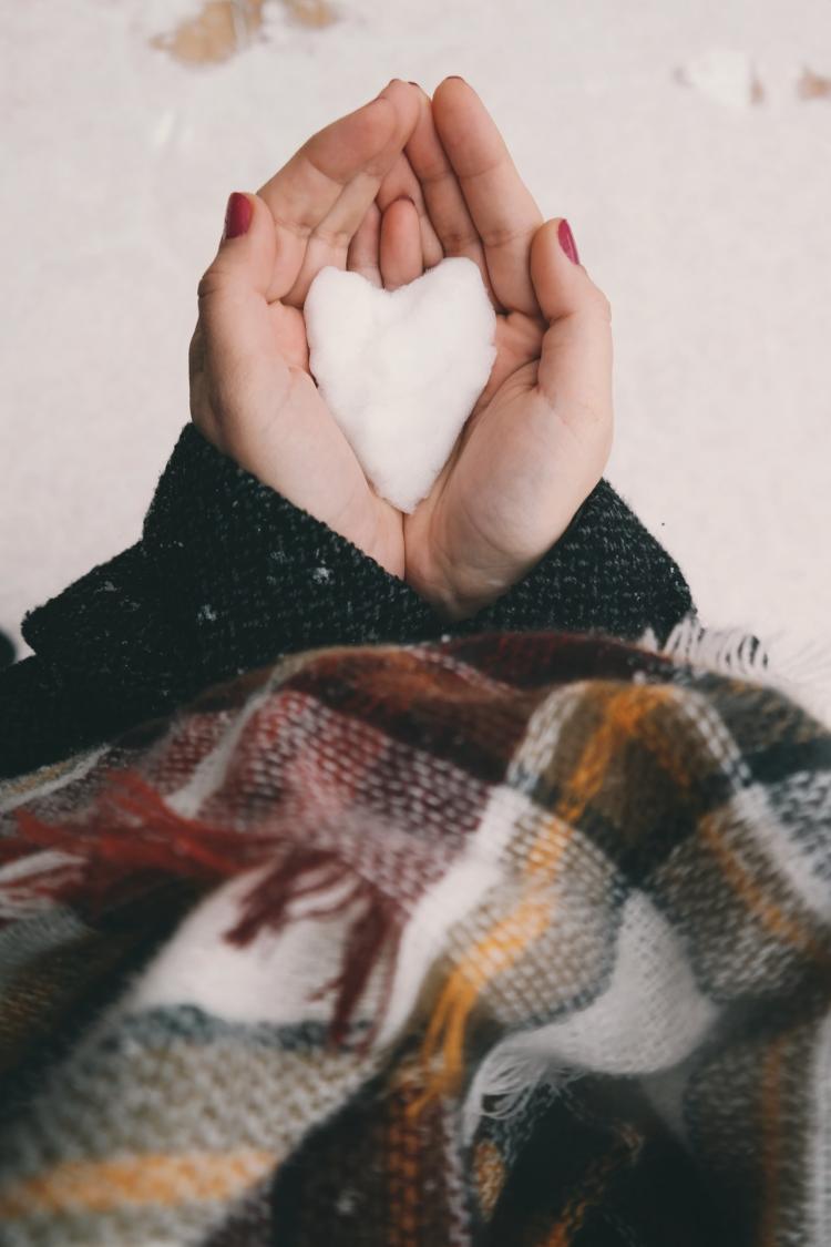 Snow in the shape of a heart sits in two hands.