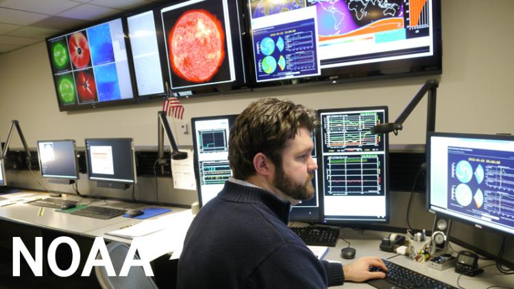 Man sits in front of rows of computer screens, some showing images of the sun