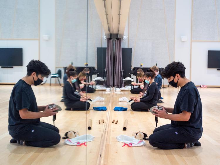 Student examines a mask while sitting in front of a mirror in a dance studio