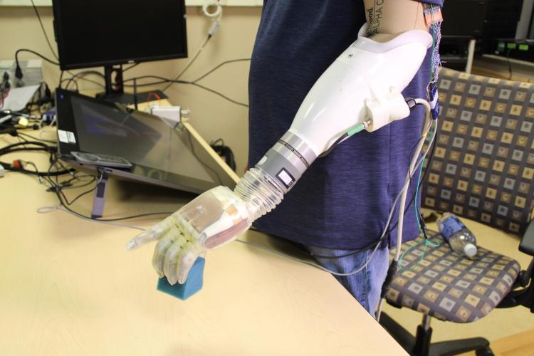 A human subject lifts a block using a feeling prosthetic.