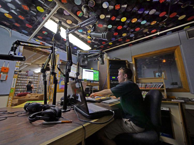 A student sits at a soundboard, operating a show in the Radio 1190 studio.