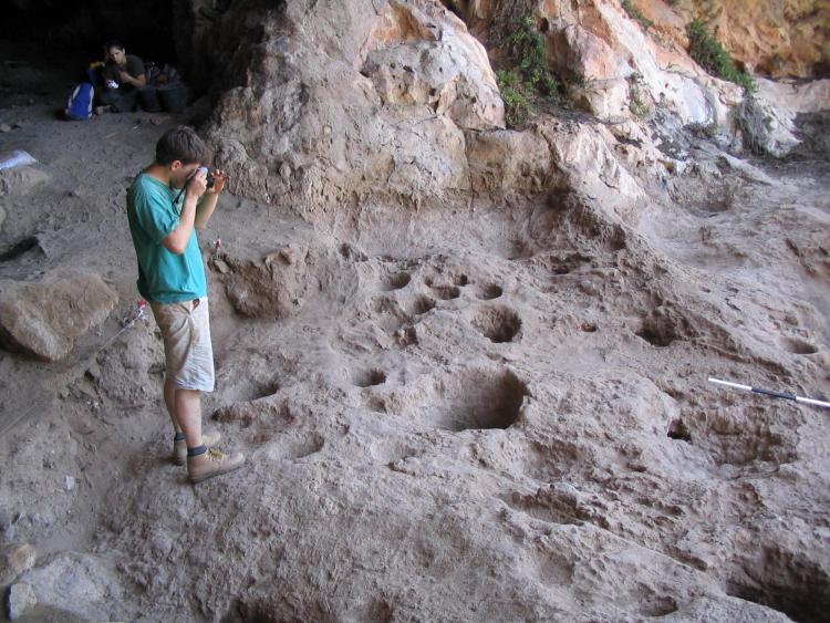 Man in a t-shirt and shorts photographs natural holes in the floor of a cave