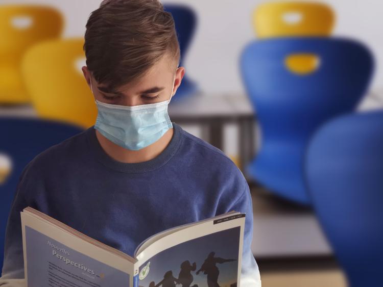Student reads book in classroom while wearing a mask.