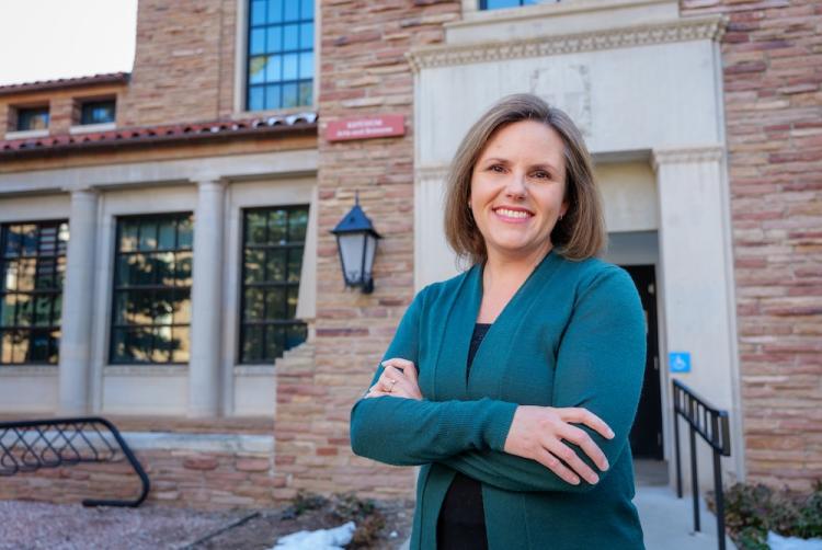 Regina Bateson stands with her arms crossed in front of a brick building