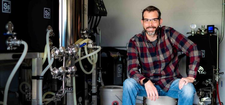 Man in flannel shirt wearing safety glasses sits next to equipment with lots of tubes