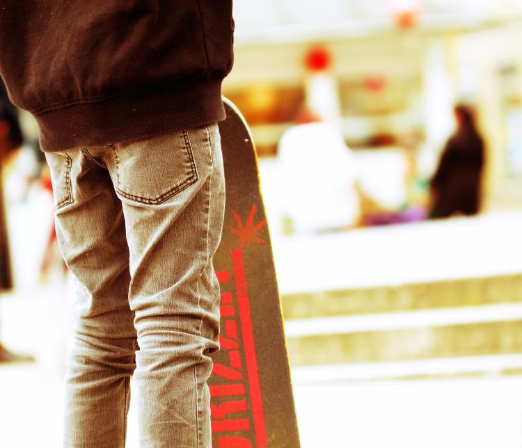 A skateboard is propped up near someone's legs, wearing jeans.
