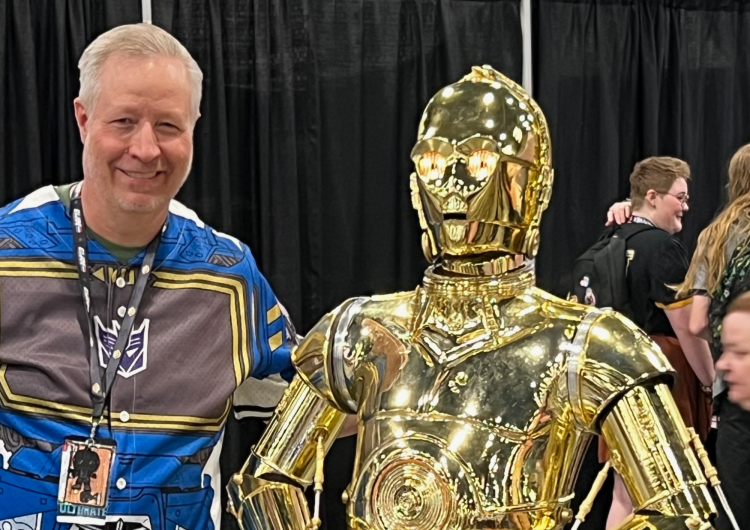 Man wearing lanyard stands next to C-3PO