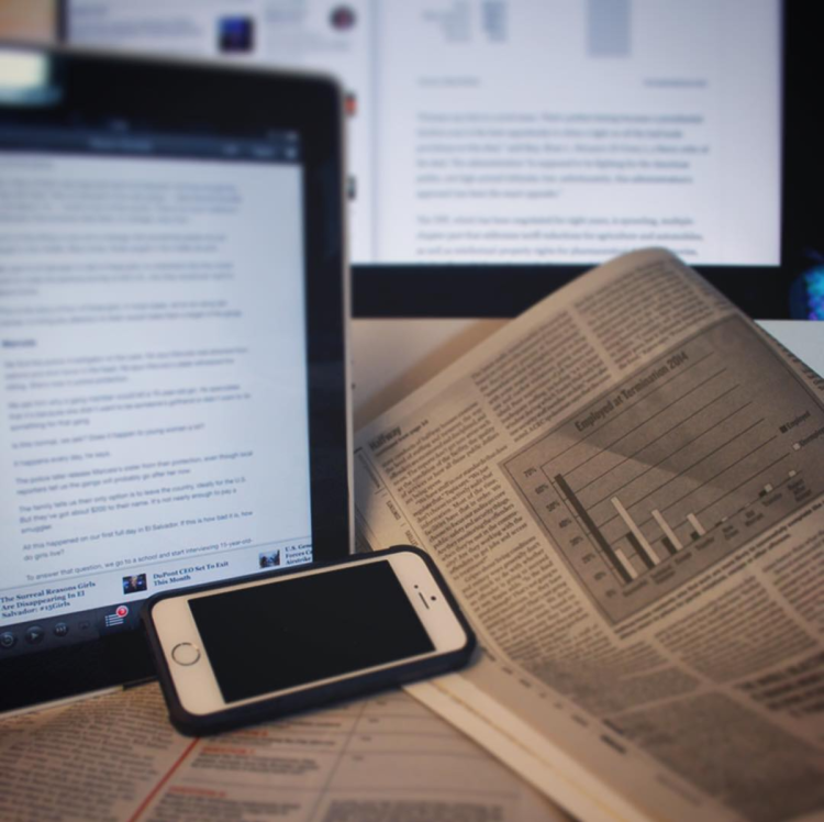 A computer monitor, smart phone and newspapers.
