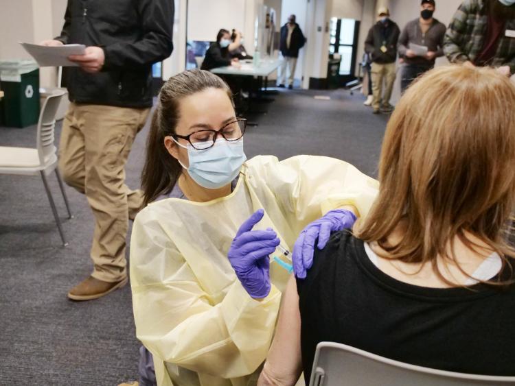 Nurse wearing face mask and shield administers a vaccine