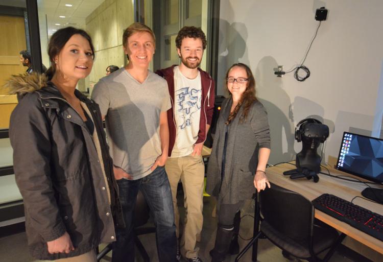 The virtual reality team stand close together in a computer room that has nice lighting.