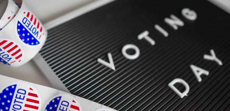 A roll of voting stickers next to a sign reading "voting day"