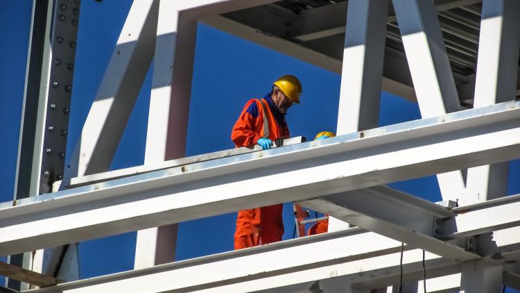 A construction worker in a helmet is seen surrounded by steel framing.