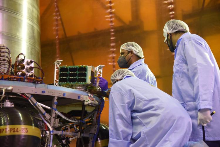Engineers in cleanroom gear load a small satellite into a rocket