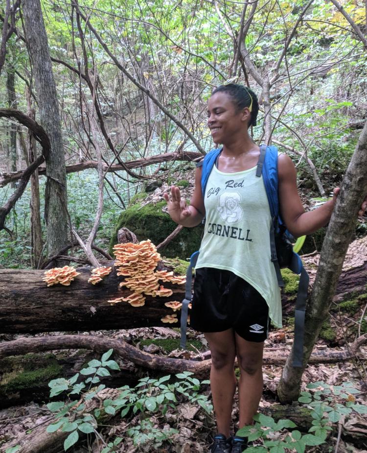 Shaz Zamore poses next to mushrooms growing on a log.