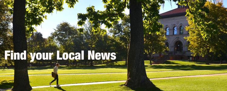 A person walks along Norlin Quad, shaded by tall trees.