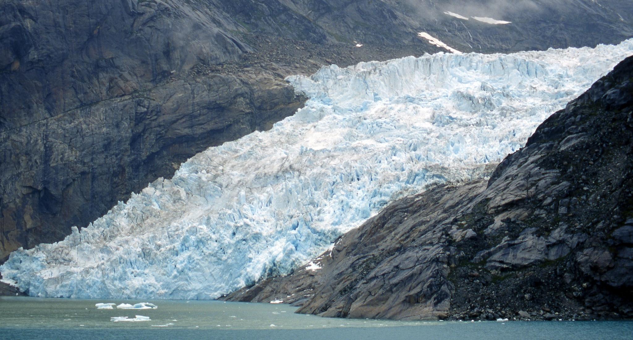 Photo of a glacier flowing through a rocky canyon into the water