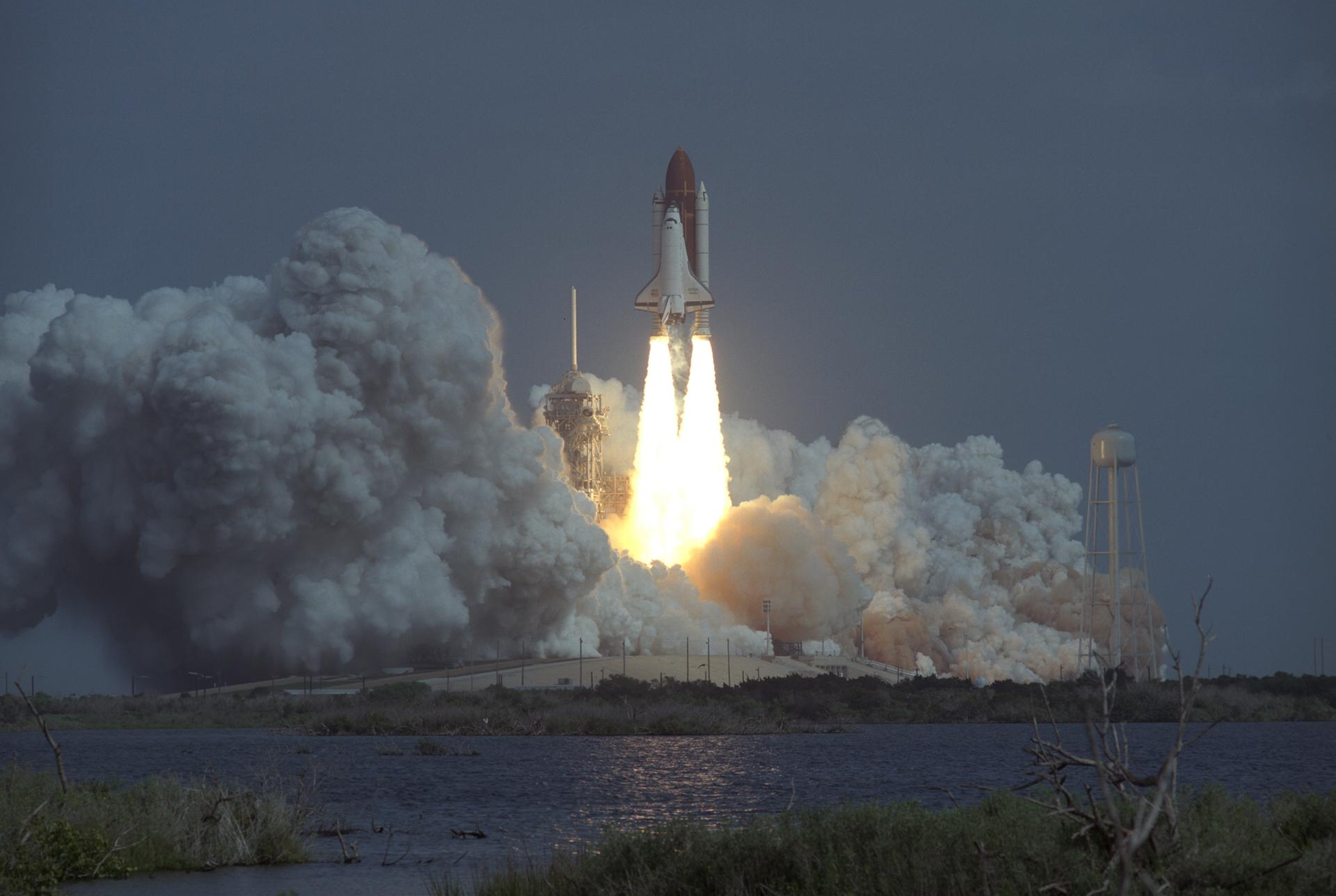 Rocket carrying space shuttle launching with exhaust billowing around it