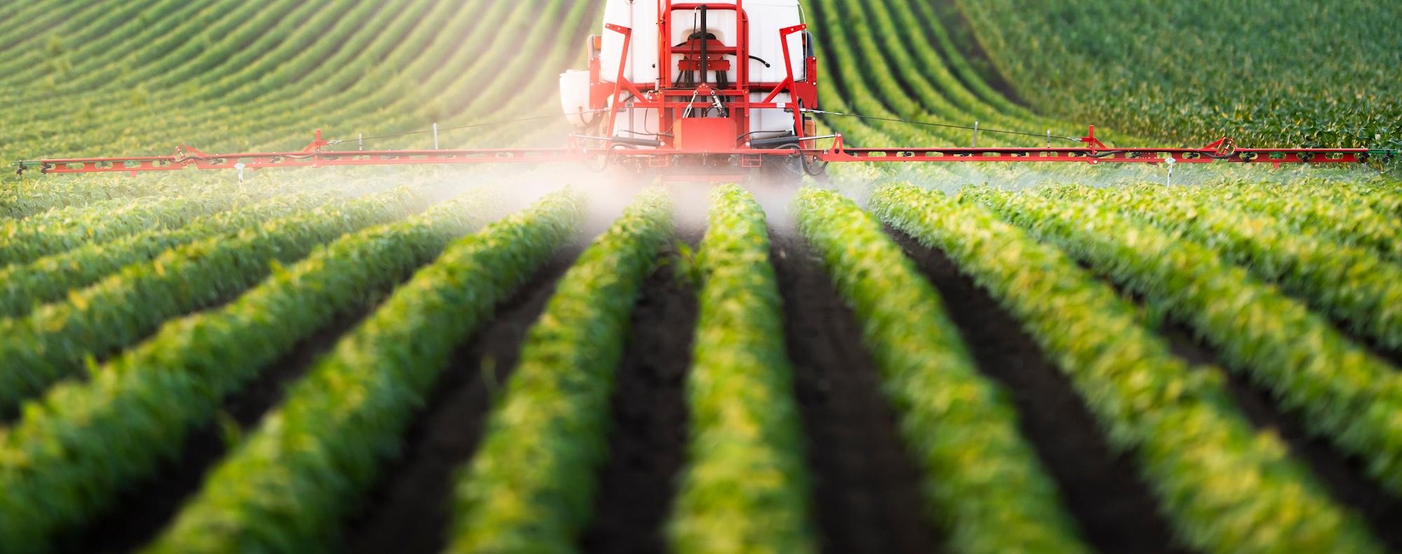 Farming vehicle sprays liquid onto rows of crops