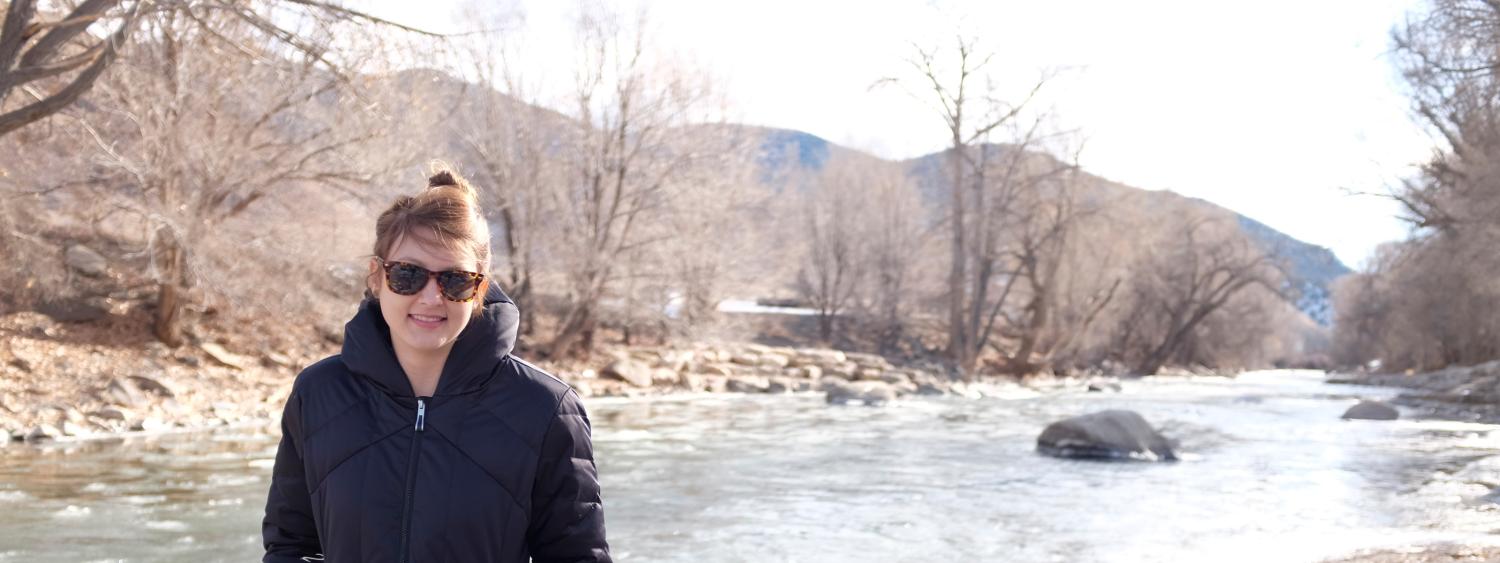 Elizabeth Koebele stands in her winter coat with the Arkansas River in the background.