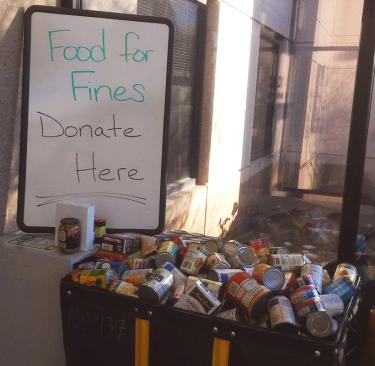 "Donate here" Food for Fines sign sits next to donated food items