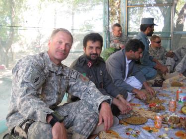 In uniform, Mitch Utterback sits cross-legged on the ground with his colleagues around a table of food.