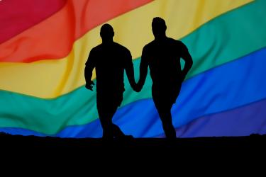 Gay male couple holding hands in front of rainbow flag background