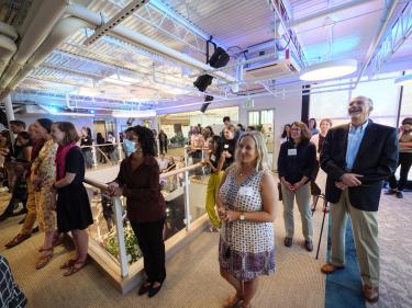Guests stand in the back of the room to listen to the event's speakers.
