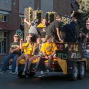 Students ride on a Homecoming float and wave to the crowd