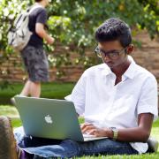 Student working on laptop, sitting in grass on campus