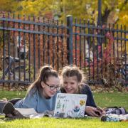 two students working at a laptop together outside