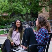 Two women sit on a bench on the CU Boulder campus.