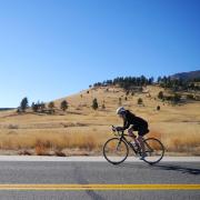 Woman bikes along highway, rolling hills