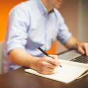 Person writing in notebook at computer