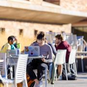 students working on laptops sitting at tables outside 