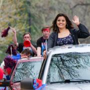 Students stick their heads out of car sunroofs as part of a car parade.