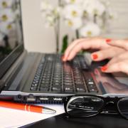 Person typing on computer, with pen and glasses nearby