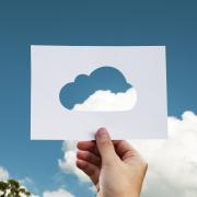 Person holds up paper cutout of cloud with sky, clouds in background