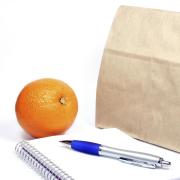 Brown-bag lunch, notebook and pen, and an orange