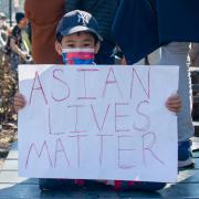 Asian American child in mask holding 'Asian Lives Matter' sign at a rally